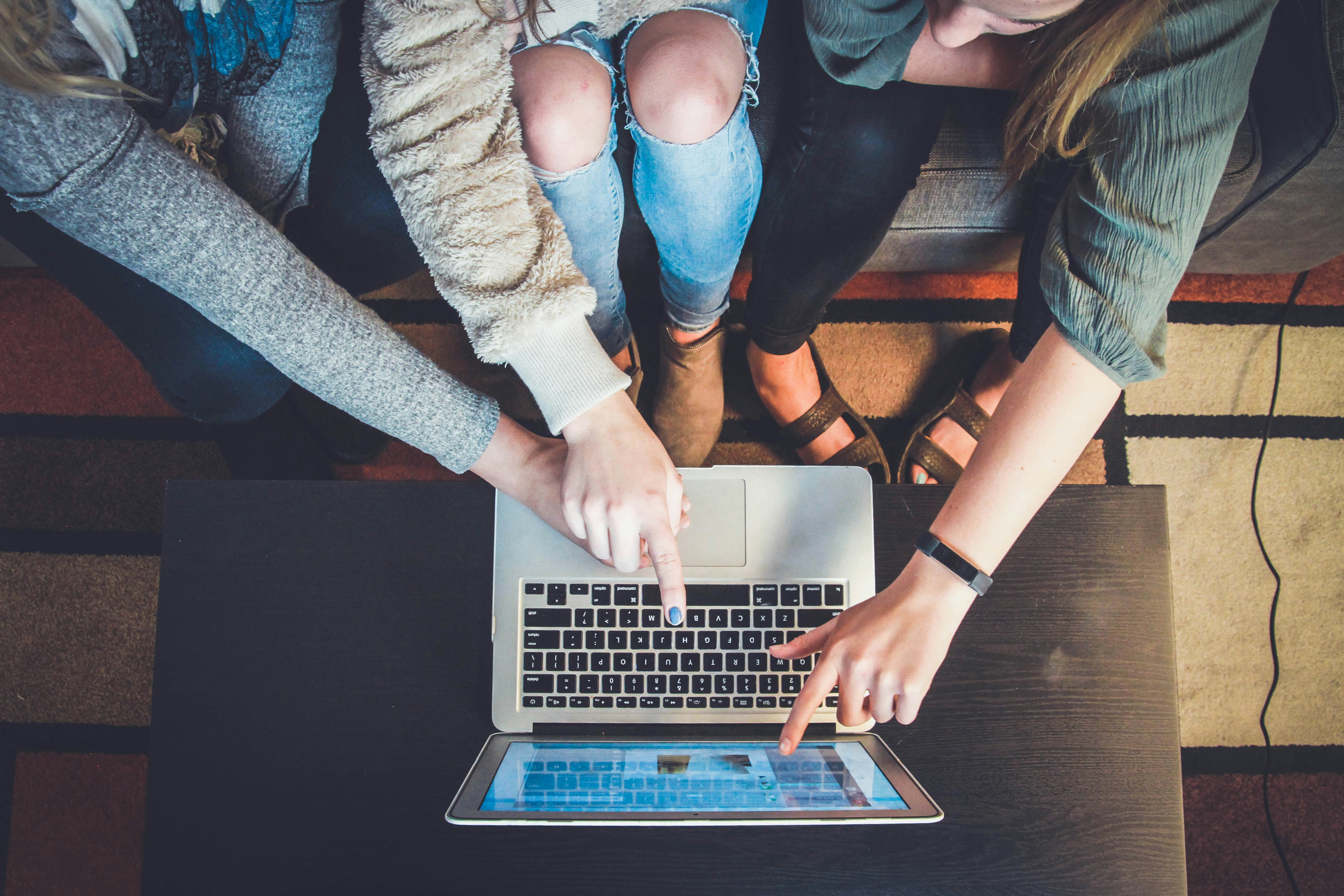 Three people pointing at a silver laptop computer.