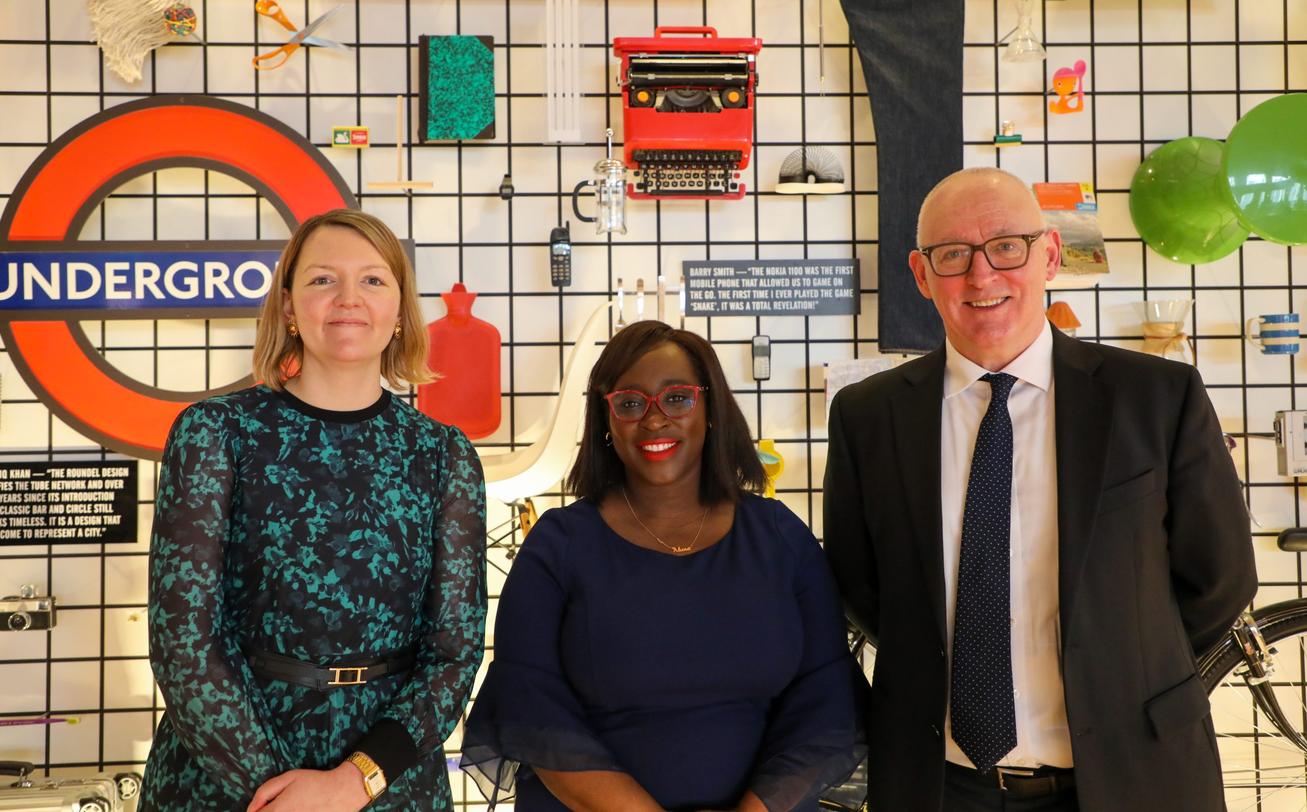 Bella Powell Cyber Director, Government Security Group, Minister Abena Oppong-Asare MP, Parliamentary Secretary at the Cabinet Office and Chief Government Security Officer Vincent Devine in front of a design display of London Underground images and icons.